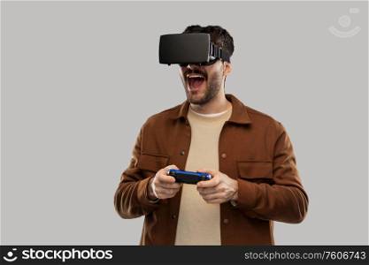 future, technology and people concept - happy smiling young man with mustaches in virtual reality headset or vr glasses with gamepad playing video game over grey background. happy smiling young man in vr glasses with gamepad