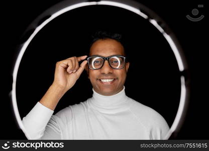 future technology, augmented reality and vision concept - indian man in glasses over white illumination on black background. man in glasses over white illumination on black