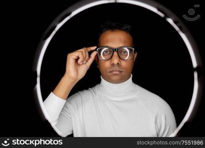 future technology, augmented reality and vision concept - indian man in glasses over white illumination on black background. man in glasses over white illumination on black