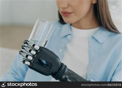 Futuristic robotic arm prosthesis. Handicapped european girl is holding glass of water with modern bionic prosthesis. High technology design artificial arm. Healthy lifestyle after&utation surgery.. High technology robotic arm prosthesis. Handicapped european girl is holding glass of water.