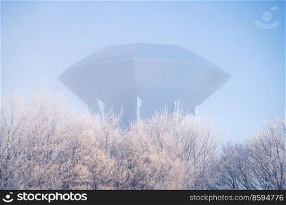 Futuristic water supply tower on cold morning with frost on the trees