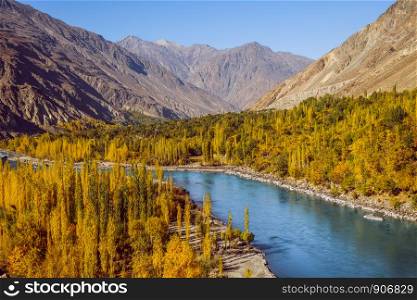 Gahkuch in autumn show river flow through colorful forest and surrounded by Hindu Kush mountain range. Ghizer valley, Gilgit Baltistan, Pakistan.