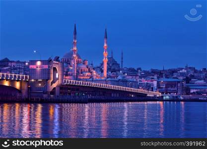 Galata Bridge and Yeni Cami Mosque in Istanbul at night. View from the embankment to the illuminated Galata Bridge and the New Mosque illuminated by electric lights. Istanbul, Turkey. Galata Bridge and Yeni Cami Mosque in Istanbul at night
