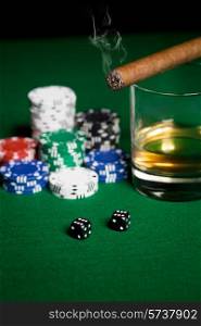 gambling, fortune and entertainment concept - close up of casino chips, whisky glass, dice and smoking cigar on green table surface
