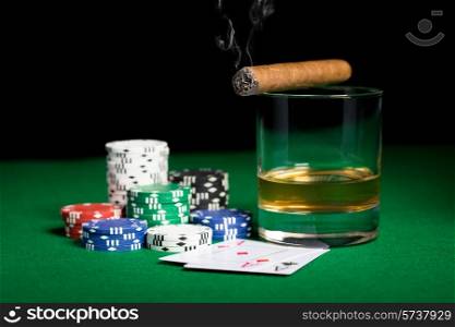 gambling, fortune and entertainment concept - close up of casino chips, whisky glass, playing cards and smoking cigar on green table surface