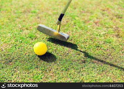 game, entertainment, sport and leisure concept - close up of metal club and ball near hole on green golf field