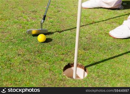 game, entertainment, sport, people and leisure concept - close up of man playing golf and putting ball with metal club into hole on golf field