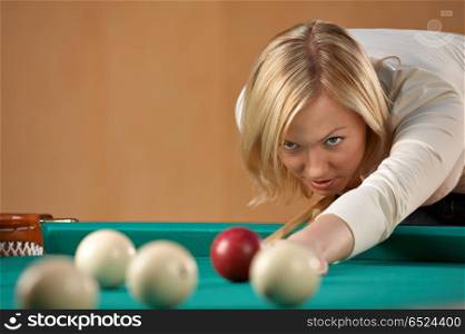 Game. The beautiful blonde aims to a sphere in billiards