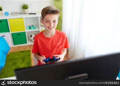gaming, technology and people concept - smiling boy with gamepad and computer playing video game at home. boy with gamepad playing video game on computer