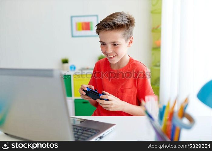 gaming, technology and people concept - smiling boy with gamepad and laptop computer playing video game at home. boy with gamepad playing video game on laptop