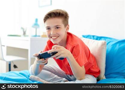 gaming, technology and people concept - smiling boy with gamepad playing video game at home. happy boy with gamepad playing video game at home