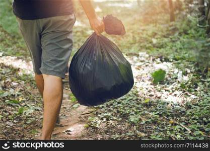 Garbage collection ecology people cleaning the park / man hand holding black plastic garbage bags in the forest , Cleaning the world Save earth concept