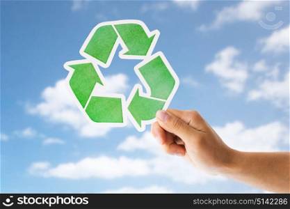 garbage disposal, environment and ecology concept - close up of hand holding green recycling sign over blue sky and clouds background. close up of hand with green recycle sign over sky