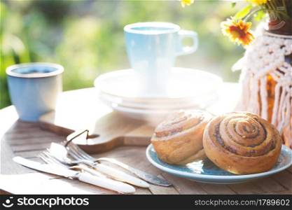 garden and tea party at the country style. still life - cinnamon rolls, cups, dishes and a vase with wildflowers