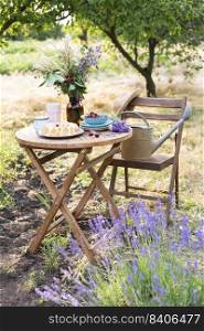 garden and tea party at the country style. still life -  herry pie, cups, dishes and a vase with wildflowers. watering can, lavender and rubber boots in the foreground 