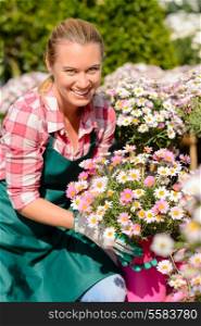 Garden center woman worker holding pink potted flowers smiling sunny