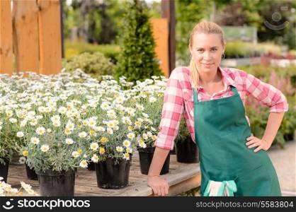 Garden center woman worker leaning against table with potted daisy flowers