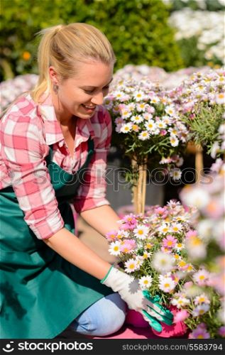 Garden center woman worker looking down daisy potted flowers sunny