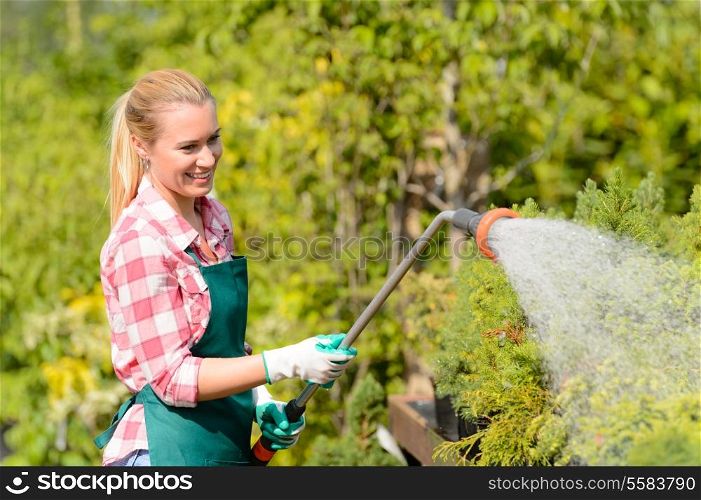 Garden center woman worker watering plants with hose smiling sunny