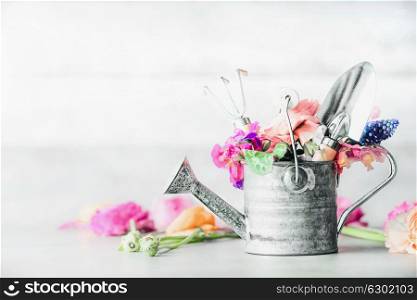 Garden set still life with watering can, gardening tools and flowers on white table, front view.