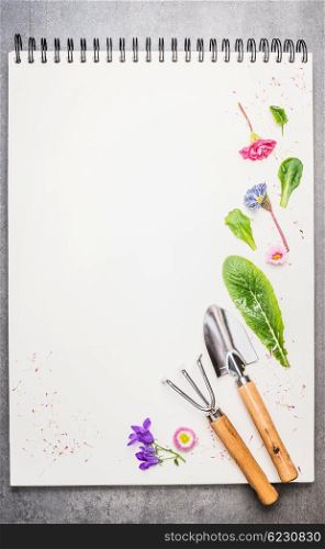 Garden tolls with flowers and petal on blank notebook. Gardening background.