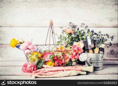 Garden tools with watering can, basket and flowers on gardening table at wooden background, front view