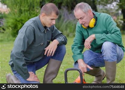 gardener and his assistant crouched beside strimmer