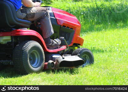 Gardener driving a riding lawn mower in a garden .. Gardener driving a riding lawn mower in a garden