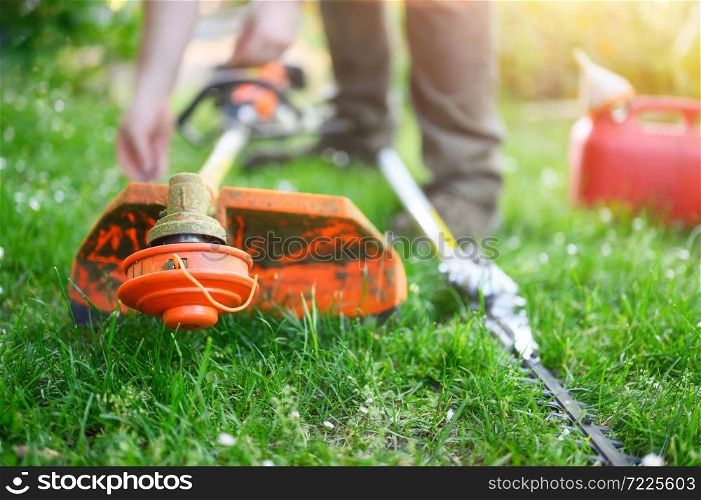 Gardener preparing grass trimmer on lawn in garden outdoors. High quality photo. Gardener preparing grass trimmer on lawn in garden outdoors.