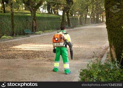 Gardener with blower backpack working in city park , blowing leaves. Autumn concept