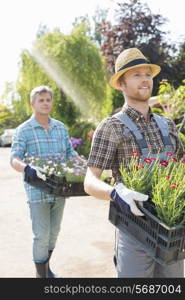 Gardeners carrying flower pots in crates at plant nursery