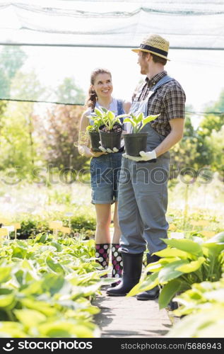 Gardeners discussing while holding potted plants at garden