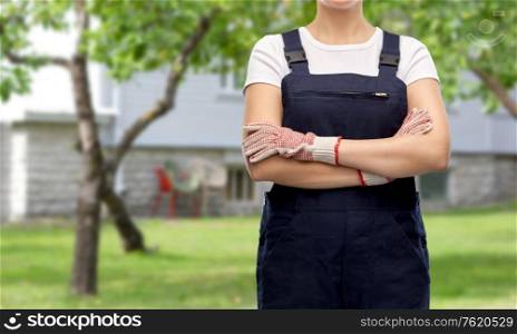 gardening and construction concept - close up of female gardener or builder in overall and gloves over living house yard background. close up of female gardener or builder in overall