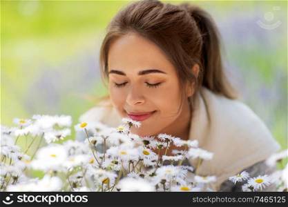 gardening and people concept - close up of happy young woman smelling chamomile flowers at summer garden. close up of woman smelling chamomile flowers
