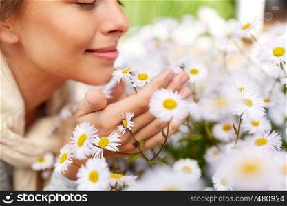 gardening and people concept - close up of happy young woman smelling chamomile flowers at summer garden. close up of happy woman smelling chamomile flowers