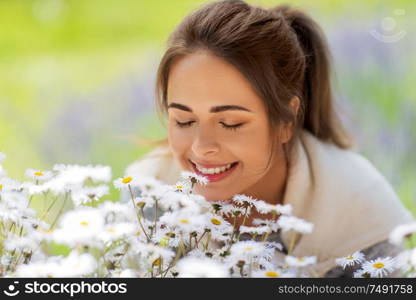 gardening and people concept - close up of happy young woman smelling chamomile flowers at summer garden. close up of woman smelling chamomile flowers