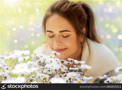 gardening and people concept - close up of happy young woman smelling chamomile flowers at summer garden. close up of woman smelling chamomile flowers