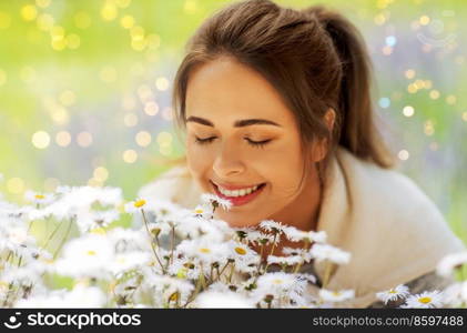 gardening and people concept - close up of happy young woman smelling chamomile flowers at summer garden. close up of woman smelling chamomile flowers