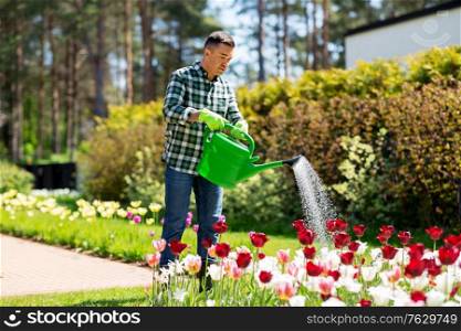 gardening and people concept - happy middle-aged man with watering can pouring water to flower bed at garden. middle-aged man watering flowers at garden