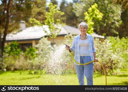 gardening and people concept - happy senior woman watering lawn by garden hose at summer. senior woman watering lawn by hose at garden. senior woman watering lawn by hose at garden