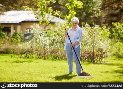 gardening and people concept - happy senior woman with lawn rake working at summer garden. senior woman with lawn rake working at garden. senior woman with lawn rake working at garden