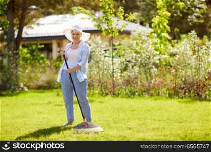 gardening and people concept - happy senior woman with lawn rake working at summer garden. senior woman with lawn rake working at garden