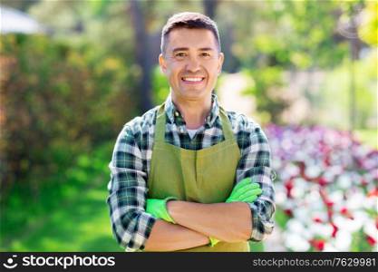 gardening and people concept - happy smiling middle-aged man in apron with crossed hands at summer garden. happy man in apron at summer garden