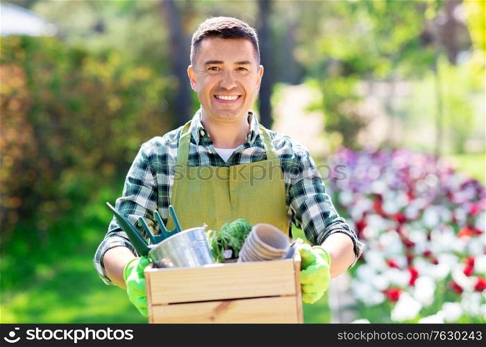 gardening and people concept - happy smiling middle-aged man in apron with tools in box at summer garden. happy man with tools in box at summer garden