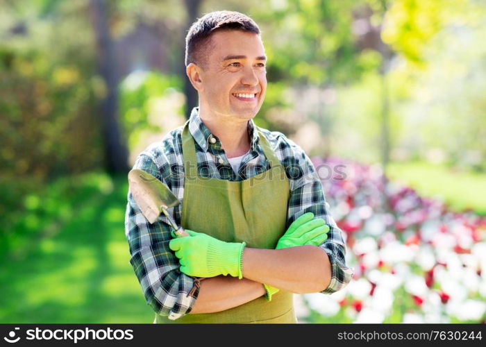 gardening and people concept - happy smiling middle-aged man in apron with scoop and crossed hands at summer garden. happy man in apron with scoop at summer garden