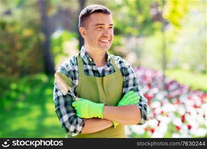 gardening and people concept - happy smiling middle-aged man in apron with scoop and crossed hands at summer garden. happy man in apron with scoop at summer garden