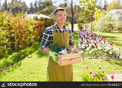 gardening and people concept - happy smiling middle-aged man in apron with tools in box at summer garden. happy man with tools in box at summer garden