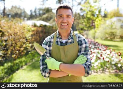 gardening and people concept - happy smiling middle-aged man in apron with trowel in crossed hands at summer garden. happy man in apron with trowel at summer garden