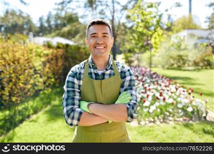 gardening and people concept - happy smiling middle-aged man in apron with crossed hands at summer garden. happy man in apron at summer garden