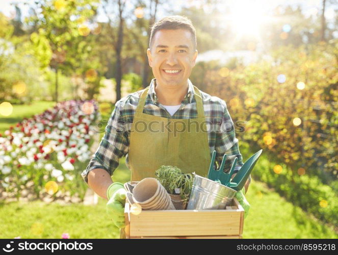 gardening and people concept - happy smiling middle-aged man in apron with tools in box at summer garden. happy man with tools in box at summer garden